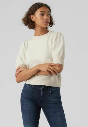 Pull en tricot couleur crème avec des manches courtes bouffantes et un col rond, associé à un jean en denim bleu marine. Texture douce et coupe décontractée.