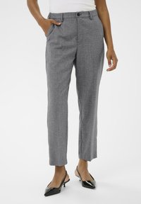 Pantalons gris ajustés avec une finition texturée, comportant des poches latérales et une fermeture à bouton à l'avant. Associés à des escarpins noirs à bout pointu.