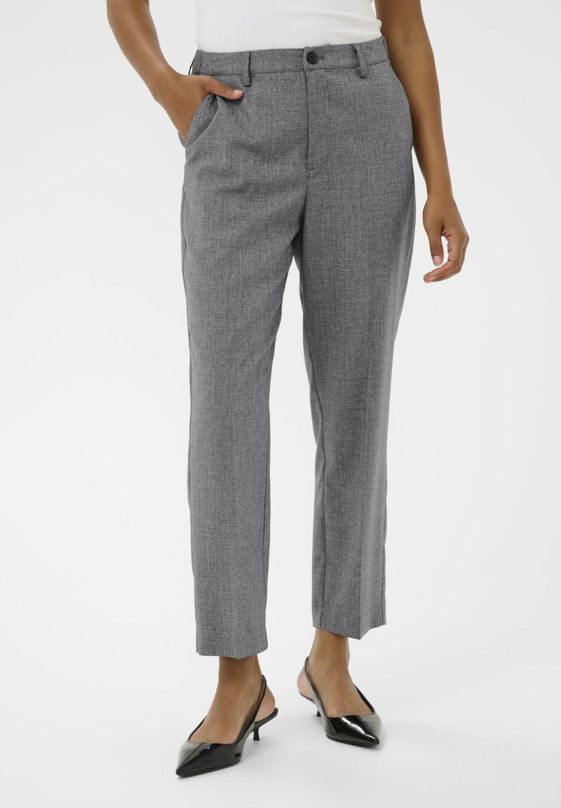 Pantalons gris ajustés avec une finition texturée, comportant des poches latérales et une fermeture à bouton à l'avant. Associés à des escarpins noirs à bout pointu.