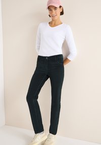 Černé kordové kalhoty se slim fit střihem a předními kapsami, v kombinaci s bílou košilí s dlouhým rukávem a růžovou čepicí, doplněné béžovými teniskami.