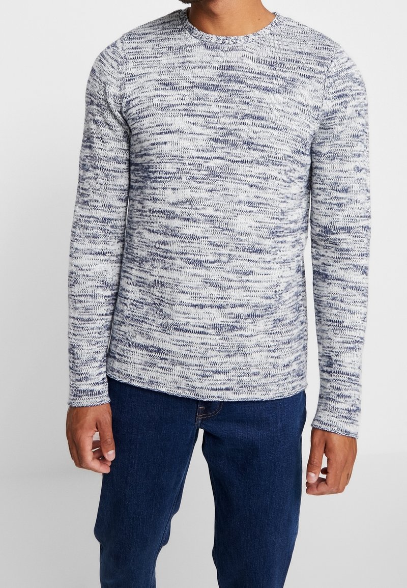 Långärmad stickad tröja med rund halsringning och ett texturerat mönster i vitt och marinblått. Tyget är mjukt; ärmarna är åtsittande och fållen är rak. Kombinerad med mörka jeans.