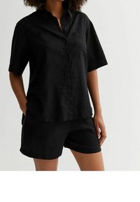 Chemise noire en lin à manches courtes avec un design à boutons, poche poitrine et coupe décontractée, associée à un short noir assorti.