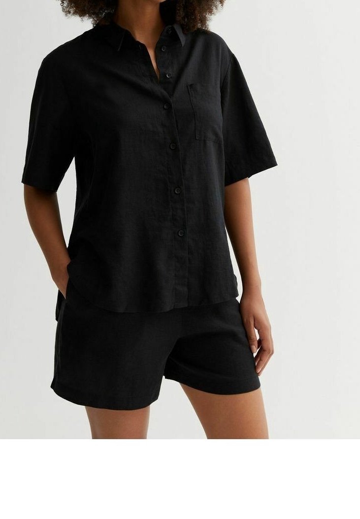 Chemise noire en lin à manches courtes avec un design à boutons, poche poitrine et coupe décontractée, associée à un short noir assorti.