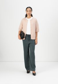 Light pink, short-sleeve cardigan with buttons, worn over a white shirt, paired with dark green wide-leg pants and black pointed shoes.