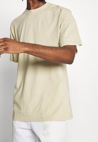 Beige bomulds t-shirt med korte ærmer, rund hals og afslappet pasform, der har minimale sømme og ingen synlige mønstre eller logoer.