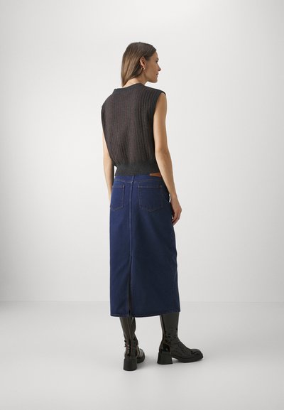 Mørk utenermet strikket topp med vertikale striper, parret med et langt marineblått denimskjørt med slitt bak og lommer, båret med skinnende svarte støvler.
