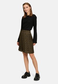 Top a maniche lunghe nero a costine con bordi ondulati abbinato a una gonna pieghettata con motivo oro e nero e scarpe nere chunky.