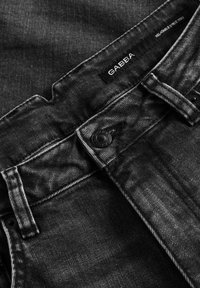 Svarta denimjeans med texturerad yta, utrustade med knappstängning, femfickorsdesign och en etikett med texten "GABBA."