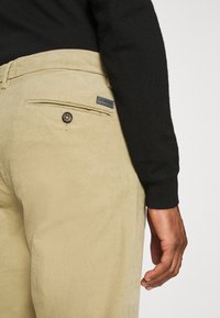 Krämfärgade manchesterbyxor med bakficka som har en svart knapp och ett varumärkesetikett. Justerad passform, texturerat tyg och subtila räfflor.