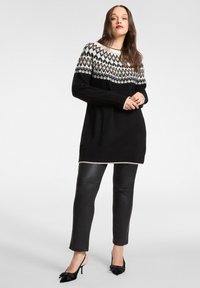 Zwarte sweaterjurk met een geometrisch breipatroon in wit en crème, met een gestructureerde stof, gecombineerd met zwarte leren broek en zwarte slingback hakken.