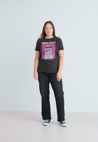 Juoda grafikė T-shirt su tekstu "BORN AGAIN", su leopardų dizainu, derinama su juodomis kelnėmis ir sportbačiais. Paprastas, kasdienis apranga.