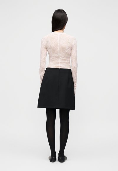 Haut en dentelle rose clair à manches longues associé à une jupe noire trapèze. La tenue comporte une fermeture éclair au dos et est complétée par des collants noirs.