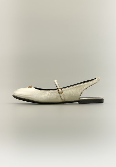 Sandale plate en cuir blanc cassé avec une fine bride et une petite boucle dorée sur le coup de pied, ainsi qu'une semelle noire basse.