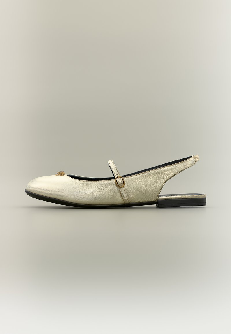 Εκρού δερμάτινο slingback φλατ με λεπτό λουράκι και μικρή χρυσή αγκράφα πάνω από τον κουντεπιέ, και χαμηλή μαύρη σόλα.