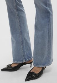 Sorte skinn slingback hæler med spisse tær og dekorative spenne detaljer, paret med lyseblå vide jeans.