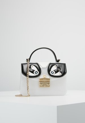 Biała torebka z czarnymi łatami w kształcie oka, złotym zapięciem, krótkim uchwytem i złotym łańcuszkowym paskiem, umieszczona na białej podstawce na jednolitym tle.