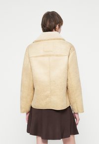 Veste en mélange de laine beige avec un col en fourrure, des manches larges et une texture lisse, dotée d'un dos plat et d'un design épuré.