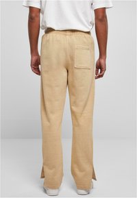Beige bredbens sweatpants med elastisk talje, baglomme og sidespalter i kanten; blød tekstur, afslappet design.