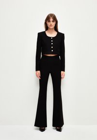 Zwarte cropped jack met grote ronde gouden knopen en een vierkante halslijn, gecombineerd met bijpassende hoogliggende flare broeken.
