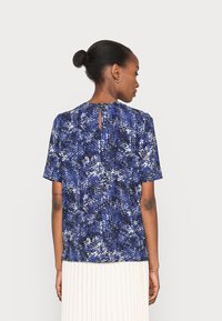 Blusa de manga curta azul com padrão, apresentando um detalhe nas costas em forma de buraco de fechadura e um corte descontraído, combinada com uma saia plissada em off-white.