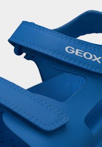 Blå Geox-sandal med justerbare borrelåsremmer og synlig merkevarelogo på den øvre remmen.