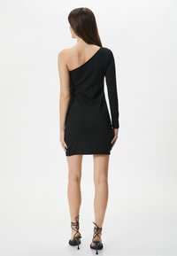 Zwarte jurk met een asymmetrisch ontwerp, voorzien van een lange mouw en een schouderloze kant. Gemaakt van zachte stof, met een aansluitende silhouet.