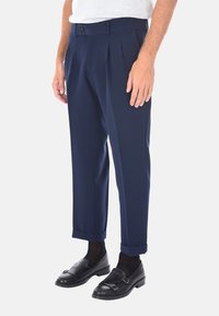 Pantaloni plissettati blu navy realizzati in tessuto liscio, con una vestibilità su misura e risvolti, abbinati a mocassini neri e calzini scuri.