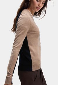 Stickad cardigan med beige framstycke och marinblå sidopanlar, med knappar, långa ärmar och ribbade muddar och nederkant. Slät textur.