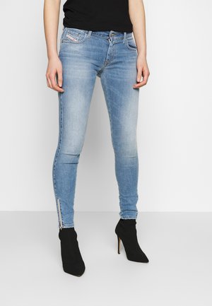 Jeans skinny de color azul claro con un lavado desgastado, detalles de cremallera en los tobillos y un diseño clásico de cinco bolsillos, combinados con botas negras de tobillo.