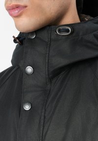 Μαύρο ελαφρύ μπουφάν με κουκούλα, διακοσμημένο με ασημένια κουμπιά και καφέ κορδόνια, λεία υφή και διακριτές ραφές.