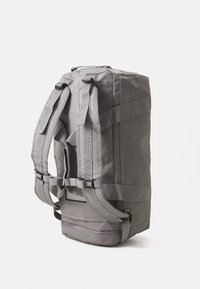 Mochila cinza com alças ajustáveis, forma retangular, tecido texturizado e um bolso com fecho na base para armazenamento extra.
