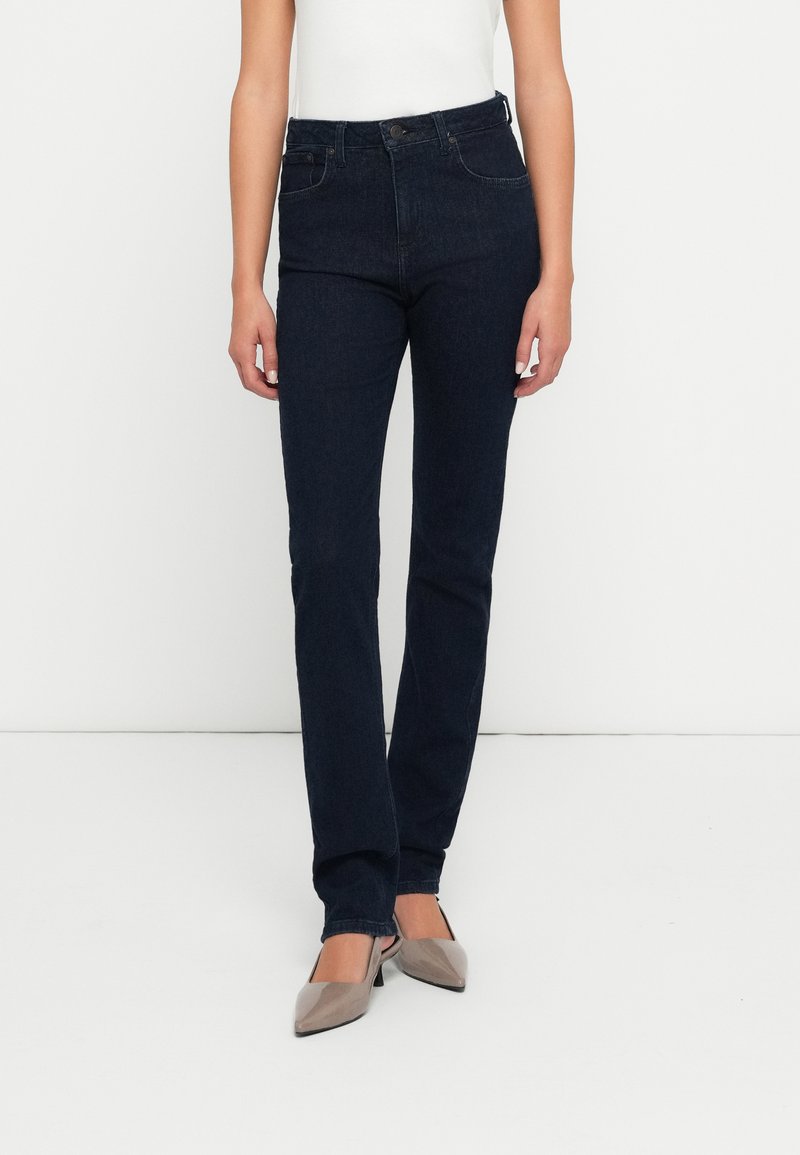 Jeans de cintura alta en azul oscuro con corte ajustado. Fabricados en denim, cuentan con un diseño clásico de cinco bolsillos y cierre de botón. Textura suave.