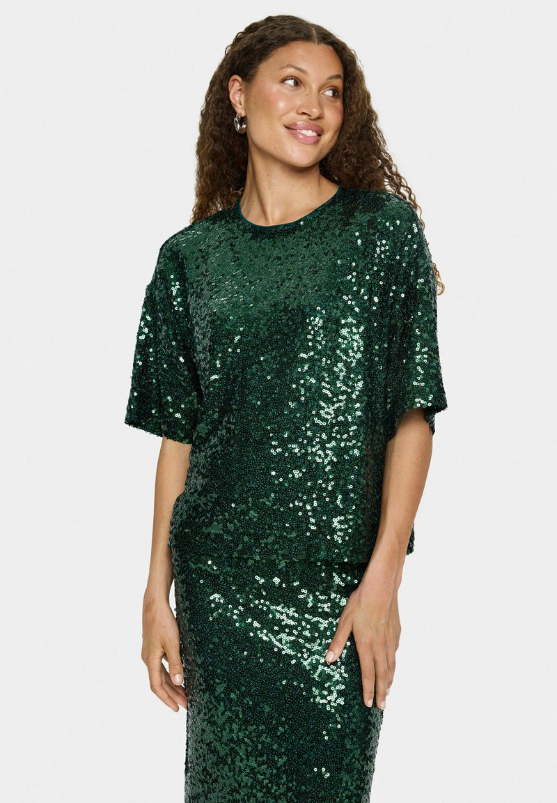 Haut vert à sequins avec des manches courtes, doté d'un col rond et d'une texture douce et brillante. Associé à une jupe à sequins assortie.