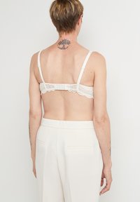 Soutien-gorge blanc en dentelle au dos, avec des bretelles réglables et une fermeture à crochet. Matière lisse avec des détails en dentelle festonnée le long du dos.