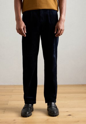 Pantaloni in corduroy blu navale con vestibilità dritta, caratterizzati da una texture a righe verticali, tasche laterali e indossati con scarpe slip-on nere.