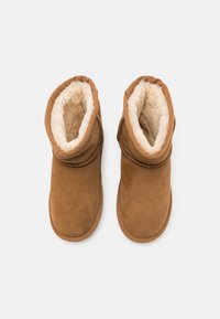 Bottines en suède marron avec une douce doublure en fourrure blanche. Elles ont un bout arrondi et un détail de revers. Semelles plates pour plus de confort.
