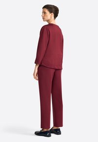 Ensemble bordeaux en deux pièces comprenant un haut ample avec des poches latérales et un pantalon droit. Tissu lisse avec des détails de couture minimaux.