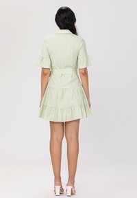 Robe rayée verte avec un corsage ajusté et une jupe à volants en cascade. Elle possède des manches courtes, un col et une ceinture assortie à la taille.