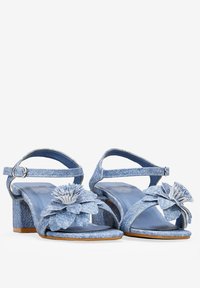 Sandalias de tacón de mezclilla azul con correa ajustable en el tobillo, correas anchas para los dedos, acentos florales y una superficie texturizada. Tacón de forma cuadrada y altura media.