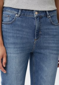 Blaue Jeans aus Denim mit schmalem Schnitt, fünf Taschen und dezentem Verblassen. Der Bund hat eine Metallknopf-Detail.