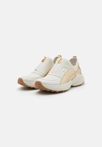 Hvite og beige slip-on sneakers med en teksturert overdel, som har glidelås og gullakenter. Gummisålen gir godt grep.