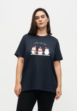 Femme portant un t-shirt sombre avec trois manchots dessinés en bande dessinée avec des bonnets de Noël et des écharpes, avec le texte "Clappy Christmas" au-dessus.