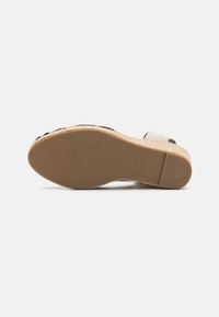 Wedge sandal with a textured beige upper and black accents. Features a natural-colored rubber sole with a patterned grip for traction.