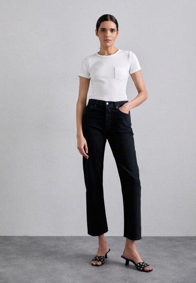 White ribbed t-shirt with a pocket, paired with high-waisted black straight-leg jeans and black heeled sandals with decorative hardware.