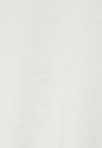 Gros plan sur un tissu en maille blanche montrant des fibres douces et texturées avec des coutures fines et de légères variations dans le motif de tissage.