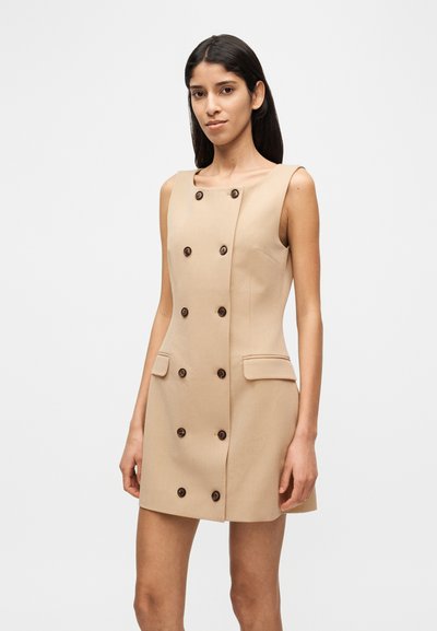 Beige ärmelloses Kleid mit Doppelknoopf-Design, Knöpfen vorne und Seitentaschen. Hergestellt aus glattem Stoff mit figurbetontem Schnitt.