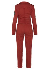 Tuta rossa con un design strutturato, maniche lunghe, spalline e vita aderente. Include una toppa circolare sul braccio sinistro.