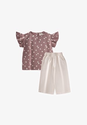 Kinderoutfit mit einem fliederfarbenen kurzärmligen Oberteil mit weißem Blumenmuster und hellbeigen weiten Hosen mit elastischem Bund.