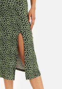 Green leopard print skirt with a mid-length design. Features a side slit for ease of movement and a smooth, textured fabric.
