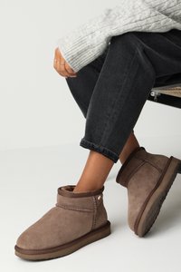 Botines de ante marrón con un suave forro interior, un diseño cosido y una suela de goma texturizada. Llevados con pantalones de mezclilla oscuros y enrollados.